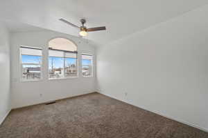 Carpeted empty room with ceiling fan and lofted ceiling