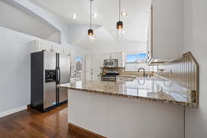 Kitchen featuring lofted ceiling, dark wood-type flooring, light stone countertops, appliances with stainless steel finishes, and white cabinetry