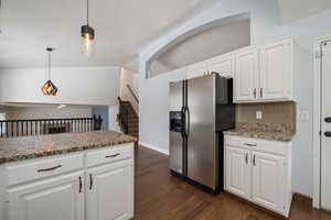 Kitchen with white cabinetry, dark wood-type flooring, stainless steel refrigerator with ice dispenser, lofted ceiling, and decorative light fixtures