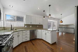 Kitchen with dark wood-type flooring, kitchen peninsula, hanging light fixtures, white cabinetry, and stainless steel appliances