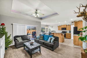 Living room with a tray ceiling, ceiling fan, sink, and light wood-type flooring