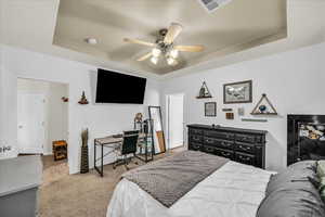 Carpeted bedroom with a raised ceiling and ceiling fan