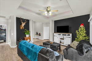 Living room with light wood-type flooring, a tray ceiling, and ceiling fan