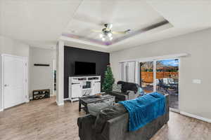 Living room with ceiling fan, a tray ceiling, and light hardwood / wood-style flooring