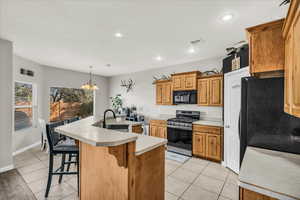 Kitchen with sink, a notable chandelier, an island with sink, a breakfast bar, and black appliances