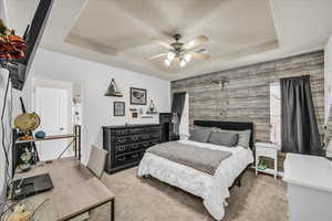 Carpeted bedroom featuring ceiling fan, a raised ceiling, and multiple windows