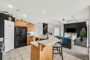 Kitchen featuring a kitchen bar, a kitchen island with sink, sink, ceiling fan, and black fridge with ice dispenser