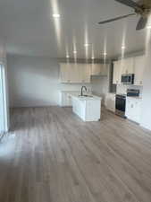 Kitchen with white cabinets, sink, light hardwood / wood-style flooring, an island with sink, and appliances with stainless steel finishes