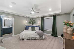 Carpeted bedroom with a tray ceiling, ensuite bath, ceiling fan, and sink