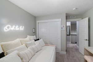 Bedroom with light colored carpet, a textured ceiling, and a closet