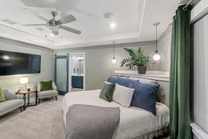 Bedroom featuring ceiling fan, a barn door, ensuite bathroom, light colored carpet, and a tray ceiling