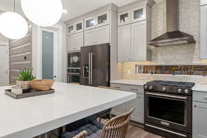 Kitchen featuring pendant lighting, wall chimney exhaust hood, gray cabinets, tasteful backsplash, and stainless steel appliances