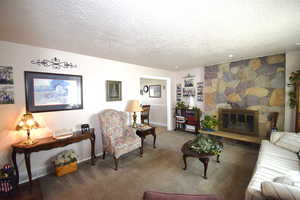 Carpeted living area featuring a fireplace, baseboards, and a textured ceiling