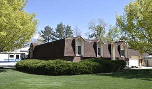 View of property exterior with a gambrel roof, a yard, an attached garage, brick siding, and roof with shingles