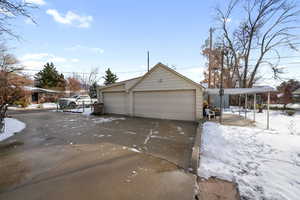 View of snowy exterior featuring an outbuilding, a garage, and a carport