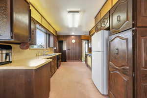 Kitchen with wooden walls, white refrigerator, sink, and light carpet