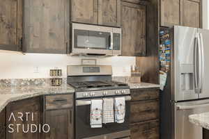 Kitchen with dark brown cabinetry, light stone countertops, and stainless steel appliances