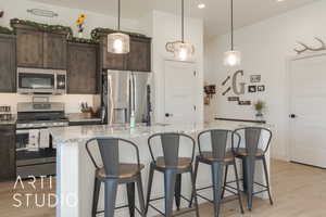 Kitchen featuring light hardwood / wood-style flooring, dark brown cabinetry, stainless steel appliances, and an island with sink