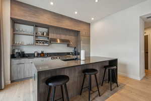 Kitchen with stainless steel microwave, sink, wall chimney exhaust hood, light hardwood / wood-style floors, and a kitchen bar