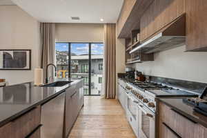 Kitchen with sink, wall chimney exhaust hood, stainless steel appliances, and light hardwood / wood-style floors