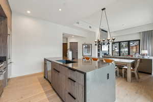 Kitchen with light wood-type flooring, decorative light fixtures, a large island, and sink