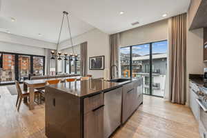 Kitchen featuring stainless steel appliances, sink, decorative light fixtures, light hardwood / wood-style floors, and an island with sink