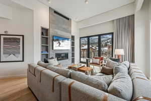 Living room with hardwood / wood-style floors, built in shelves, a towering ceiling, and a tile fireplace