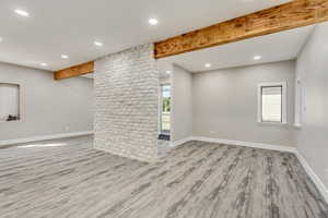 Unfurnished living room featuring beam ceiling and light hardwood / wood-style floors