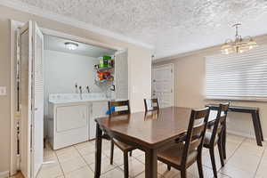 Dining area featuring ornamental molding, a textured ceiling, washer and dryer, light tile patterned floors, and an inviting chandelier