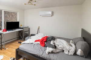 Bedroom with a wall mounted air conditioner, wood-type flooring, and a baseboard radiator