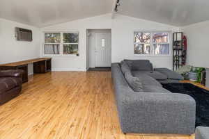 Living room featuring vaulted ceiling with beams, wood-type flooring, and a wall mounted AC