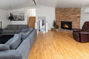 Living room with a wall mounted air conditioner, lofted ceiling, a stone fireplace, rail lighting, and hardwood / wood-style flooring