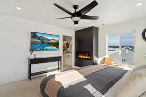 Carpeted bedroom featuring a large fireplace, ceiling fan, and connected bathroom