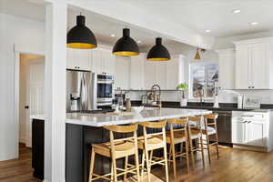 Kitchen with hanging light fixtures, light hardwood / wood-style flooring, beamed ceiling, white cabinets, and appliances with stainless steel finishes