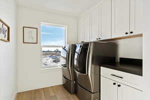 Laundry room with washing machine and dryer, cabinets, and light wood-type flooring