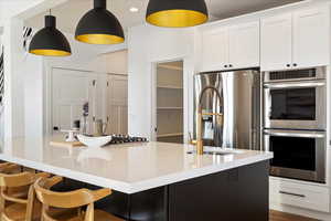 Kitchen featuring white cabinetry, light stone countertops, decorative light fixtures, and appliances with stainless steel finishes