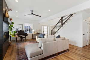 Living room with ceiling fan, a large fireplace, and light wood-type flooring