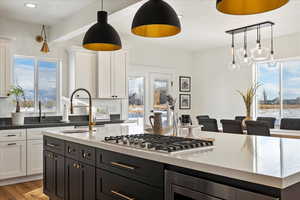 Kitchen with white cabinetry, sink, stainless steel gas cooktop, light hardwood / wood-style flooring, and pendant lighting