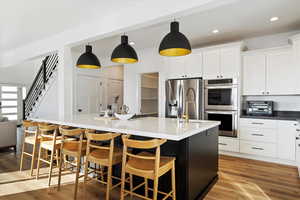 Kitchen featuring light hardwood / wood-style flooring, stainless steel appliances, hanging light fixtures, and an island with sink