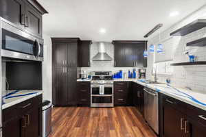 Kitchen featuring dark hardwood / wood-style flooring, wall chimney exhaust hood, stainless steel appliances, and decorative light fixtures