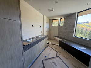 Bathroom featuring tiled shower, dual sinks, and tile walls