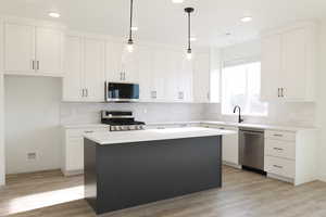 Kitchen with decorative light fixtures, light hardwood / wood-style floors, a kitchen island, white cabinets, and appliances with stainless steel finishes