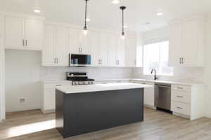 Kitchen with appliances with stainless steel finishes, white cabinetry, a center island, and decorative light fixtures