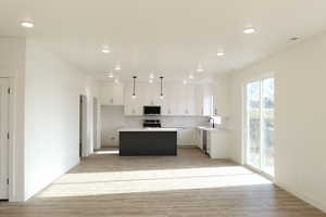 Kitchen featuring stainless steel appliances, a center island, white cabinets, decorative light fixtures, and sink