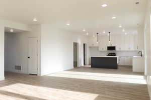 Kitchen featuring stainless steel appliances, white cabinetry, backsplash, hanging light fixtures, and a kitchen island