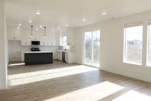 Kitchen with decorative light fixtures, white cabinets, a kitchen island, and stainless steel appliances