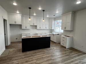 Kitchen featuring white cabinetry, hardwood / wood-style floors, a kitchen island, and pendant lighting