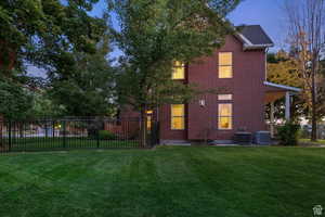 Back house at dusk with a lawn and central AC