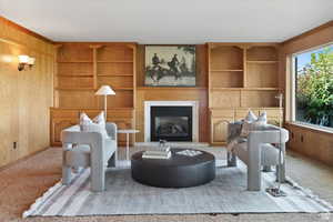 Living room featuring light carpet, built in features, and wooden walls