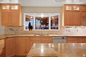 Kitchen featuring dishwasher, light stone counters, sink, and tasteful backsplash